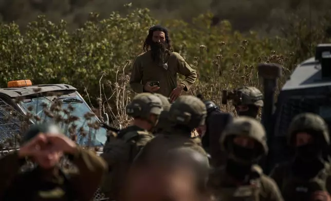 FILE - An Israeli settler overlooks members of Israeli forces blocking a road preventing Palestinians from reaching groves to harvest olives in the West Bank town of Turmus Ayya, Oct. 21, 2026. (AP Photo/Leo Correa, File)