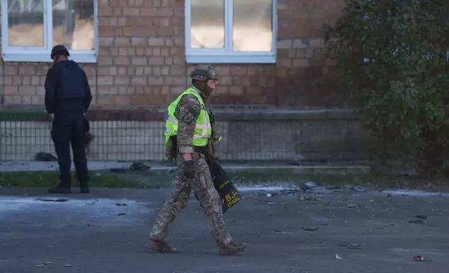 A police officer carries fragments of a Shahed drone in front of a school damaged by a Russian strike in Kyiv, Ukraine, Thursday, Oct. 1, 2026. (AP Photo/Evgeniy Maloletka)