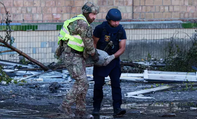 A police officer and a rescue worker carry an unexploded warhead from a Shahed drone out of a school damaged by a Russian strike on Kyiv, Ukraine, Thursday, Oct. 1, 2026. (AP Photo/Evgeniy Maloletka)