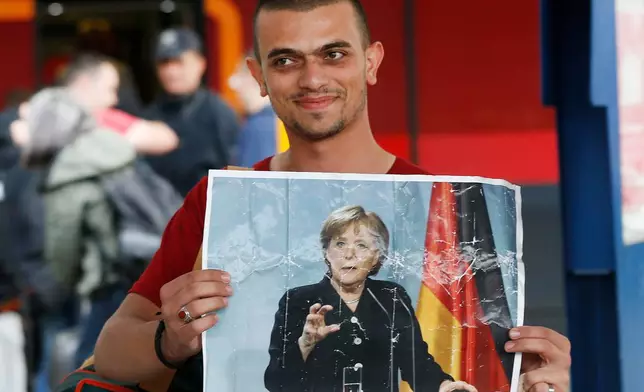 FILE - In this Sept. 5, 2015 file photo a migrant carries a picture of German Chancellor Angela Merkel as he arrives at the main train station in Munich, Germany. (AP Photo/Michael Probst, file)