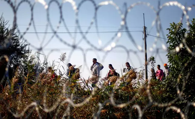 FILE - Migrants arrive at the Hungarian border fence between Serbia and Hungary near Roszke, southern Hungary, on Sept. 13, 2015. (AP Photo/Matthias Schrader, File)