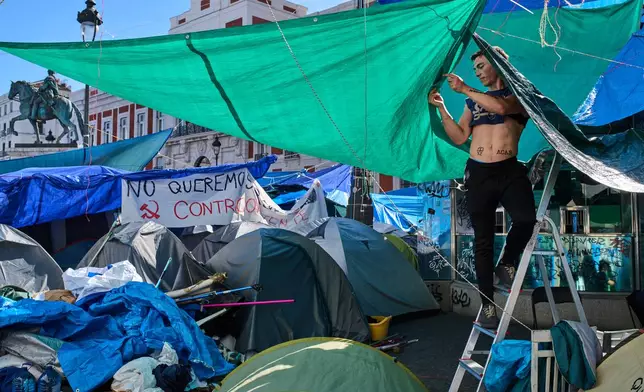 A man sets up a roof cover at a makeshift camp set up by protesters demanding stronger laws to protect renters in Puerta del Sol square in Madrid, Spain, Friday, Oct. 16, 2026. (AP Photo/Bernat Armangue)