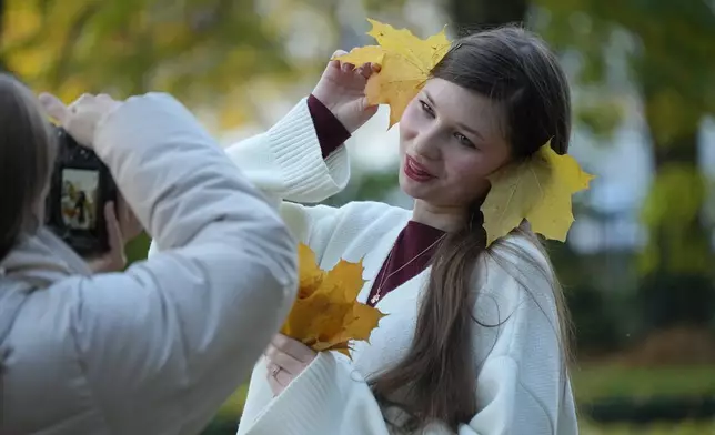 A girl poses for a photo with fallen leaves in the Summer Garden in St. Petersburg, Russia, Thursday, Oct. 15, 2026. (AP Photo/Dmitri Lovetsky)
