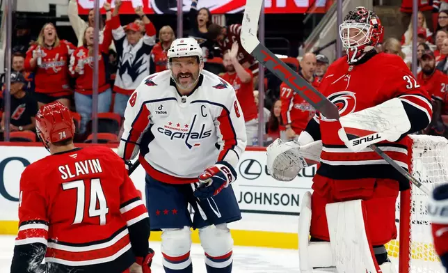 Washington Capitals' Alex Ovechkin (8) smiles as he picks up the puck for Alex Tuch (not shown) between Carolina Hurricanes' Jaccob Slavin (74) and goaltender Brandon Bussi (32) during the first period of an NHL hockey game in Raleigh, N.C., Friday, Oct. 2, 2026. (AP Photo/Karl DeBlaker)