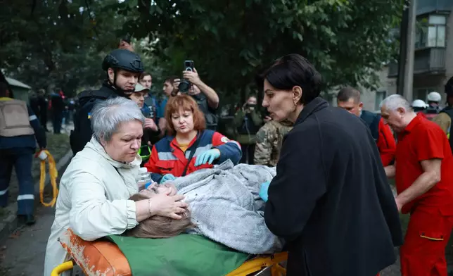 A relative speaks to a woman on a stretcher after pulling her and her husband from the rubble of a residential building destroyed by a Russian airstrike in Zaporizhzhia, Ukraine, Saturday, Oct. 10, 2026. (AP Photo/Kateryna Klochko)