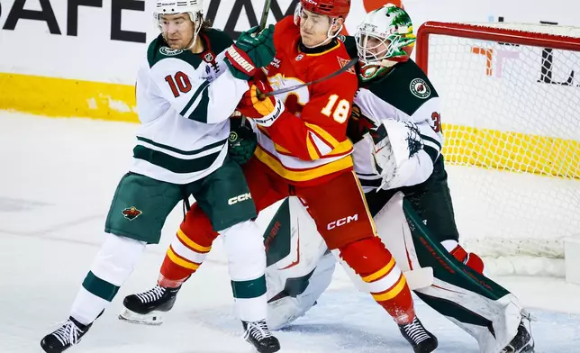 Minnesota Wild's Bobby Brink, left, checks Calgary Flames' Ben Jones, center, as Wild goalie Jesper Wallstedt, right, looks on during the second period of an NHL hockey game in Calgary, Alberta, Thursday, Oct. 22, 2026. (Jeff McIntosh/The Canadian Press via AP)