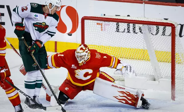 Minnesota Wild's Matt Boldy, second from right, jumps out of the way of the puck as Calgary Flames goalie Devin Cooley defends the net during the third period of an NHL hockey game in Calgary, Alberta, Thursday, Oct. 22, 2026. (Jeff McIntosh/The Canadian Press via AP)