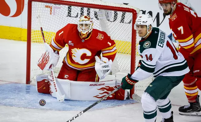 Minnesota Wild's Joel Eriksson Ek (14) looks on as Calgary Flames goalie Devin Cooley, left, looks for the puck during the third period of an NHL hockey game in Calgary, Alberta, Thursday, Oct. 22, 2026. (Jeff McIntosh/The Canadian Press via AP)