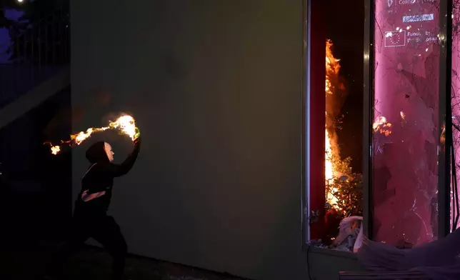 A hooded protester throws a petrol bomb at the College of Europe office during clashes in Tirana, Albania, Wednesday, Oct. 14, 2026, as students joined the Flamingo anti-government movement. (AP Photo/Hameraldi Agolli)