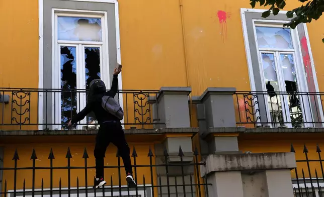 A hooded protester throws a stone toward the Education Ministry during clashes in Tirana, Albania, Tuesday, Oct. 13, 2026, joining a demonstration organized by the Flamingo protest movement demanding the resignation of Prime Minister Edi Rama. (AP Photo/Hameraldi Agolli)