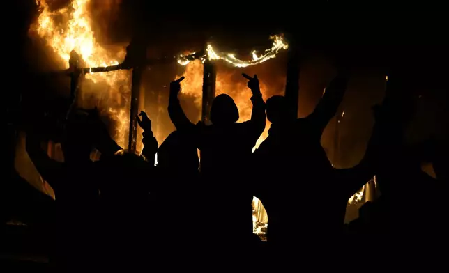 EDS NOTE: OBSCENITY - A hooded protester raises his middle fingers as fire engulfs the Justice Ministry during a violent escalation of anti-government unrest in Tirana, Albania, Wednesday, Oct. 14, 2026. (AP Photo/Hameraldi Agolli)
