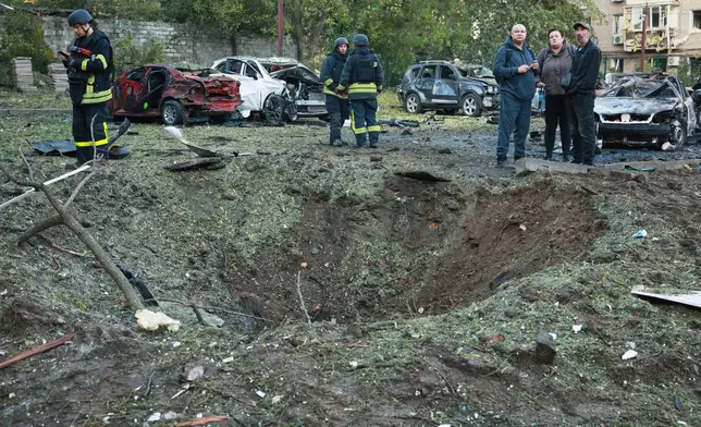 Local residents and emergency workers stand near a crater made by a Russian strike on residential neighbourhood in Zaporizhzhia, Ukraine, Friday, Oct. 9, 2026. (AP Photo/Kateryna Klochko)