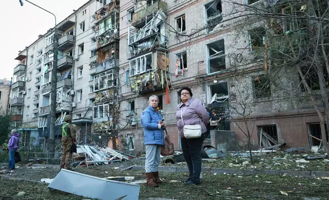 Local residents stand in front of building damaged by a Russian strike on residential neighbourhood in Zaporizhzhia, Ukraine, Friday, Oct. 9, 2026. (AP Photo/Kateryna Klochko)