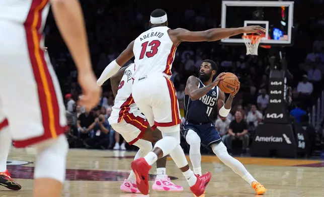 Dallas Mavericks guard Kyrie Irving (11) looks for an opening defended by Miami Heat guard Davion Mitchell (2) and center Bam Adebayo (13) during the first half of an NBA basketball game, Monday, Oct. 26, 2026, in Miami. (AP Photo/Rebecca Blackwell)