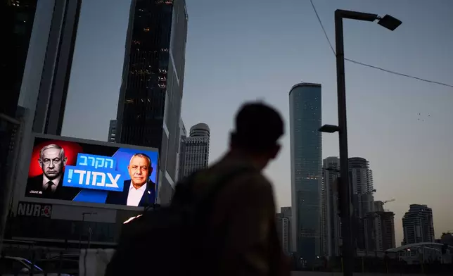 A pedestrian passes a campaign billboard featuring Israeli Prime Minister Benjamin Netanyahu, left, and his main rival, opposition candidate Gadi Eisenkot, with a message in Hebrew that reads "The race is tight," Friday, Oct. 23, 2026, in Tel Aviv, Israel. (AP Photo/David Goldman)