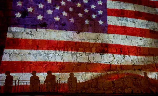 FILE - Pedestrians are silhouetted against a projection of the American flag on the walls of Jerusalem's Old City, July 5, 2026, displayed in honor of the 250th anniversary of U.S. independence. (AP Photo/Ohad Zwigenberg, File)