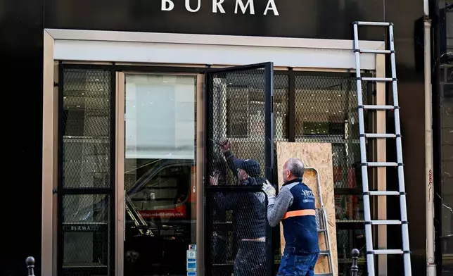 Worker install safeguards on a shop before protests over living costs and education in Paris, France, Saturday, Oct. 31, 2026. (AP Photo/Emma Da Silva)