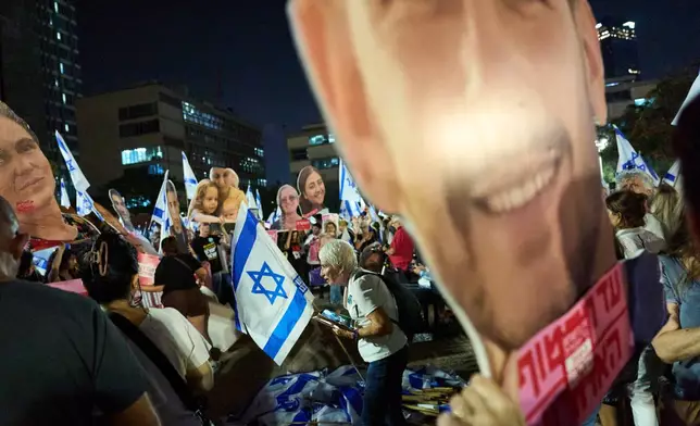 A demonstrator picks up an Israeli flag surrounded by photos of victims of Hamas' Oct. 7 attack during an anti-government protest ahead of Israel's general election, Saturday, Oct. 24, 2026, in Tel Aviv, Israel. (AP Photo/David Goldman)