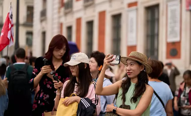Tourists take pictures of protesters camping during a protest at Sol Square following the eviction last Wednesday of 87-year-old Maricarmen as they demand stronger laws to protect renters in Madrid, Spain, Monday, Sept. 28, 2026. (AP Photo/Manu Fernandez)