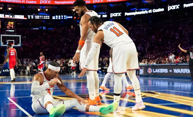 New York Knicks' Josh Hart, left, sits on the court after being fouled by Philadelphia 76ers' LeBron James (not shown) as teammates Karl-Anthony Towns, center, and Jalen Brunson, right, look to help him up during the second half of an NBA Cup basketball game, Friday, Oct. 30, 2026, in Philadelphia. (AP Photo/Chris Szagola)