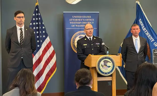 In this photo taken with a smartphone, Elija Rain, the assistant commissioner of the British Columbia Royal Canadian Mounted Police, speaks to the media on Tuesday, Oct. 6, 2026, in Seattle. Standing next to Rain are Mike Herrington, the FBI special agent in charge, left, and Acting U.S. Attorney Neil Floyd, right. (AP Photo/Manuel Valdes)