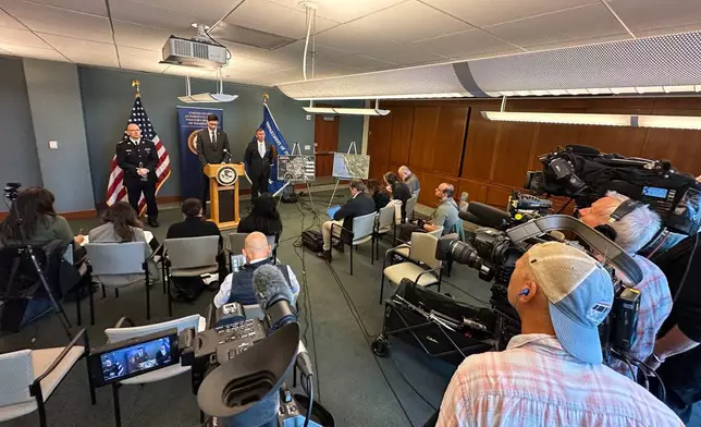 In this photo taken with a smartphone, Mike Herrington, the FBI special agent in charge, speaks to the media on Tuesday, Oct. 6, 2026, in Seattle. Standing next to Herrington are Elija Rain, the assistant commissioner of the British Columbia Royal Canadian Mounted Police, left, and Acting U.S. Attorney Neil Floyd, right. (AP Photo/Manuel Valdes)