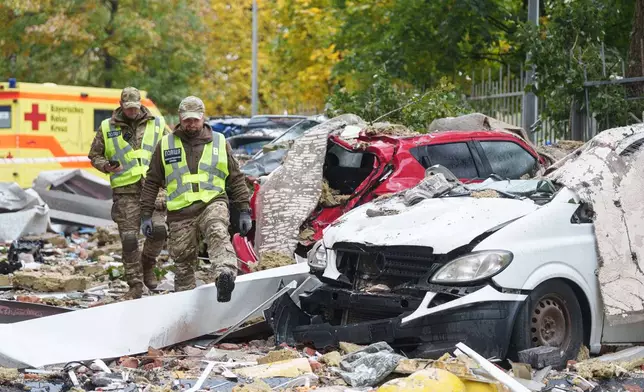 Policemen walk in front of destroyed cars in the yard of a multi-storey residential building damaged by a Russian drone strike on Kyiv, Ukraine, Wednesday, Oct. 21, 2026. (AP Photo/Evgeniy Maloletka)