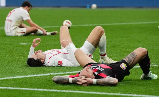 Leverkusen's Aleix Garcia and Freiburg's Igor Matanovic lie exhausted on the pitch after the German Bundesliga soccer match between Bayer Leverkusen and SC Freiburg in Leverkusen, Germany, Sunday, Oct. 18, 2026. (AP Photo/Martin Meissner)