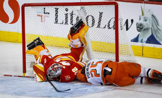 Anaheim Ducks' Ryan Poehling, right, crashes into the net knocking over Calgary Flames goalie Dustin Wolf during the third period of an NHL hockey game in Calgary, Alberta, Alberta, Saturday, Oct. 10, 2026. (Jeff McIntosh/The Canadian Press via AP)