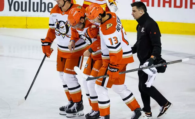 Anaheim Ducks' Ryan Poehling, center, is helped off the ice by teammates Tristan Luneau, left, and Nikita Nesterenko after crashing into the net following his goal during the third period of an NHL hockey game against the Calgary Flames in Calgary, Alberta, Alberta, Saturday, Oct. 10, 2026. (Jeff McIntosh/The Canadian Press via AP)