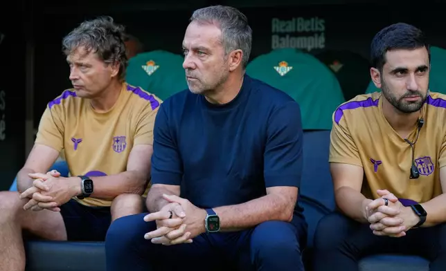 Barcelona's head coach Hansi Flick, centre, waits for the start of the Spanish La Liga soccer match between Real Betis and Barcelona in Seville, Spain, Saturday, Oct. 17, 2026. (AP Photo/Jose Breton)