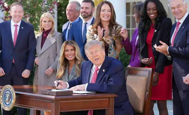 President Donald Trump, seated right with first lady Melania Trump, signs an executive order during an event about women's health, in the Rose Garden of the White House, Monday, Oct. 19, 2026, in Washington. (AP Photo/Alex Brandon)