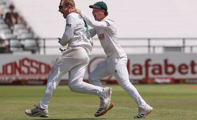 South Africa's Simon Harmer is congratulated by South Africa's Matthew Breetzke for his sixth wicket of the day on day five of the third cricket test match between South Africa and Australia, in Cape Town, South Africa, Saturday, Oct. 31, 2026. (AP Photo/Halden Krog)