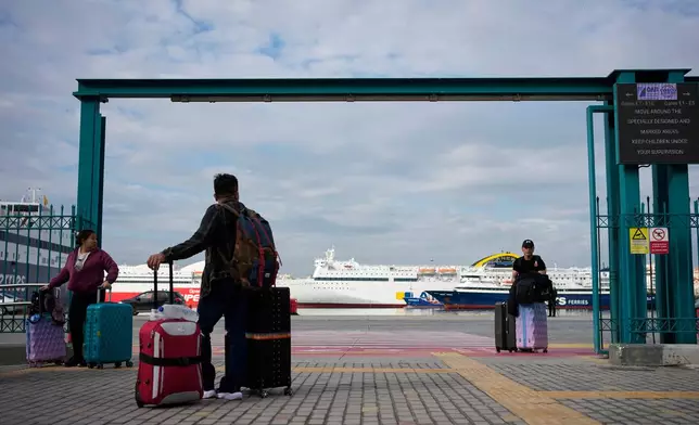 Passengers walk through the port of Piraeus during a 24-hour seafarers' strike over pay, working conditions and safety, alongside protests by port workers against the transport of military equipment through ports, near Athens, Greece, Friday, Oct. 30, 2026. (AP Photo/Thanassis Stavrakis)