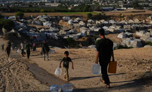 Displaced Palestinians carry water containers near a tent camp in Deir al-Balah, central Gaza Strip, Wednesday, Oct. 7, 2026. (AP Photo/Abdel Kareem Hana)