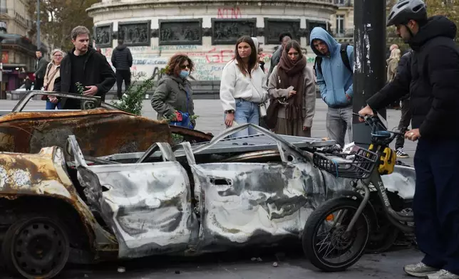 People watch a burned-out car after a quiet night Monday under curfew, the first since weekend protests over the cost of living turned into rioting and looting across France, in Paris, Tuesday, Oct. 20, 2026. (AP Photo/Christophe Ena)