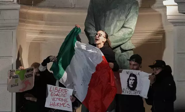 Demonstrators gather around a statue of Giuseppe Colombo, a former Italian finance minister, outside the Polytechnic University of Milan, Italy, Saturday, Oct. 24, 2026, to protest against the rising cost of living and deteriorating public services, during one of several demonstrations organized across Italy by groups spanning the political spectrum. (AP Photo/Antonio Calanni)