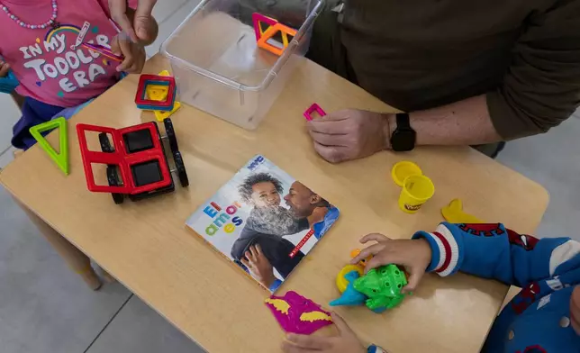 A teacher and children play with magnetic building tiles and modeling clay beside a children’s book titled El amor es at the John Cardinal O’Connor Center for Parent and Child Development, a Head Start center operated by The New York Foundling, in San Juan, Puerto Rico, Tuesday, Oct. 13, 2026. (AP Photo/Alejandro Granadillo)