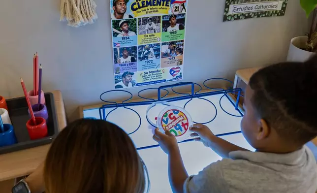 A child works with numbers beside a teacher, in front of a Spanish-language poster about Roberto Clemente, the baseball Hall of Fame inductee at the John Cardinal O'Connor Center for Parent and Child Development, a Head Start center operated by The New York Foundling, in San Juan, Puerto Rico, Tuesday, Oct. 13, 2026. (AP Photo/Alejandro Granadillo)