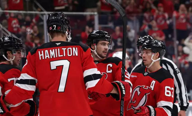 New Jersey Devils center Nico Hischier (13) is congratulated by Jesper Bratt (63) and Dougie Hamilton (7) after scoring a goal during the second period of an NHL hockey game against the Vancouver Canucks, Saturday, Oct. 10, 2026, in Newark, N.J. (AP Photo/Adam Hunger)