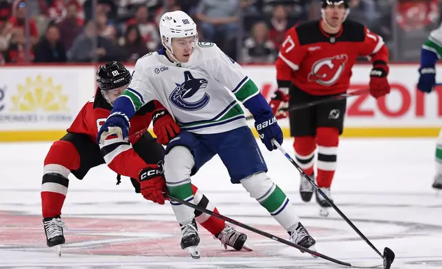 Vancouver Canucks right wing Jonathan Lekkerimaki (88) has the puck knocked away by New Jersey Devils right wing Arseny Gritsyuk during the first period of an NHL hockey game Saturday, Oct. 10, 2026, in Newark, N.J. (AP Photo/Adam Hunger)