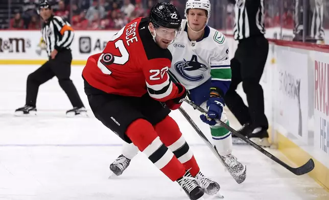 New Jersey Devils defenseman Brett Pesce (22) keeps his eyes on the puck in front of Vancouver Canucks center Marco Rossi during the first period of an NHL hockey game Saturday, Oct. 10, 2026, in Newark, N.J. (AP Photo/Adam Hunger)
