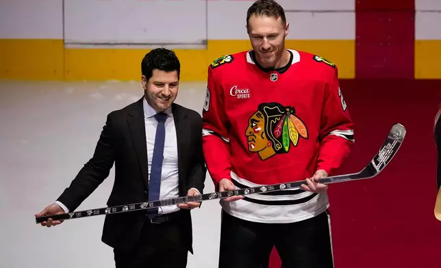 Chicago Blackhawks general manager Kyle Davidson, left, presents Chicago Blackhawks defenseman Ian Cole, right, with a silver stick for playing in his 1000th NHL game prior to an NHL hockey game against the Florida Panthers, Sunday, Oct. 25, 2026, in Chicago. (AP Photo/Harry Figiel)