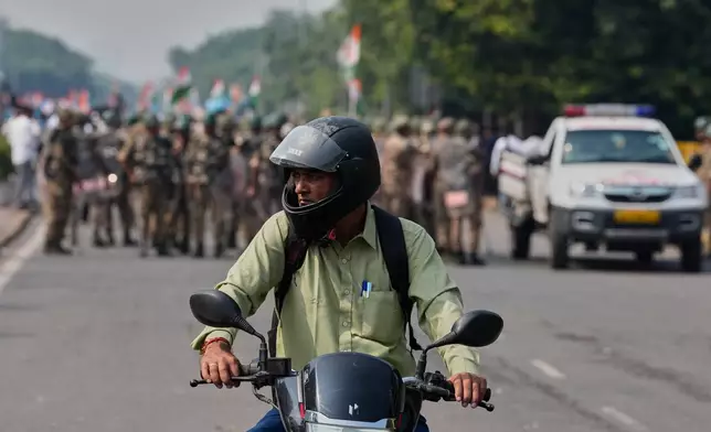 A commuter watches as security personnel arrive to escort workers of India's opposition Congress party gathering for a march toward the Supreme Court to demand the resignation of Chief Election Commissioner Gyanesh Kumar in New Delhi, India, Monday, Oct. 12, 2026. (AP Photo/Manish Swarup)