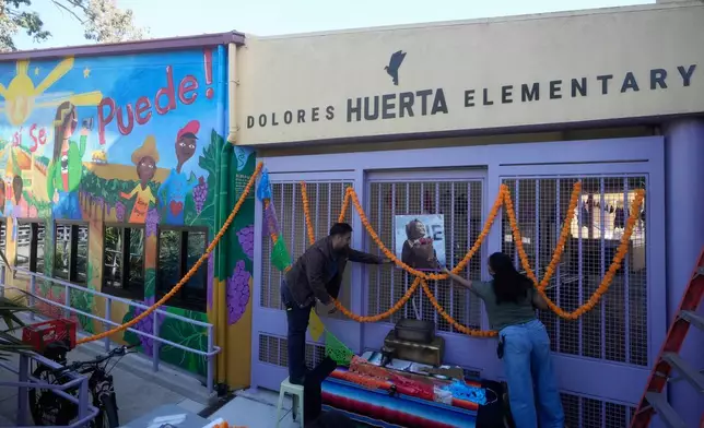 Dolores Huerta Elementary School community schools coordinator Alejandro Cuevas, left, and family liaison Magali Ramirez work on a tribute to Huerta at the entrance of the school, Wednesday, Oct. 28, 2026, in San Francisco. (AP Photo/Jeff Chiu)