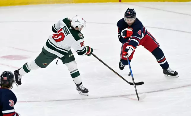 Winnipeg Jets' Neal Pionk (4) deflects a shot by Minnesota Wild's Bobby Brink (10) during first period NHL hockey action in Winnipeg, Manitoba, Tuesday, Oct. 13, 2026. (Fred Greenslade/The Canadian Press via AP)
