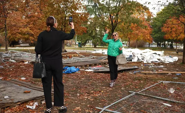 Women take photos backdropped by debris in a park used as a camp by supporters of the right-wing Serbian Progressive Party (SNS) where tents and vehicles were set on fire by celebrating crowds after Aleksandar Vucic, the party leader conceded defeat in the parliamentary election, held on Sunday, in Belgrade, Serbia, Monday, Oct. 26, 2026. (AP Photo/Armin Durgut)