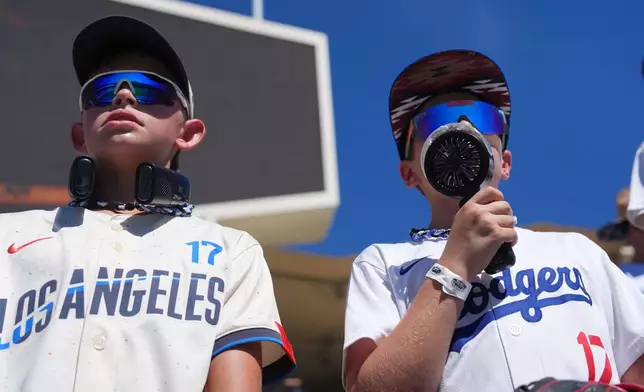 Los Angeles Dodgers fans hold electronic fans as the heat soars during batting practice before Game 1 of a National League Division Series baseball game Saturday, Oct. 3, 2026, in Los Angeles. (AP Photo/Jae C. Hong)
