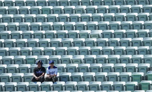Los Angeles Dodgers fans look on among empty seats as they shield themselves from the sun and heat before Game 1 of a National League Division Series baseball game against the Atlanta Braves Saturday, Oct. 3, 2026, in Los Angeles. (AP Photo/Jae C. Hong)