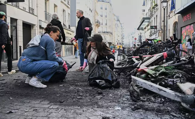 People clean up debris in a street next to burned bicycles the day after a demonstration against rising living costs and in solidarity with students' grievances, in Paris, Sunday, Oct. 18, 2026. (AP Photo/Emma Da Silva)